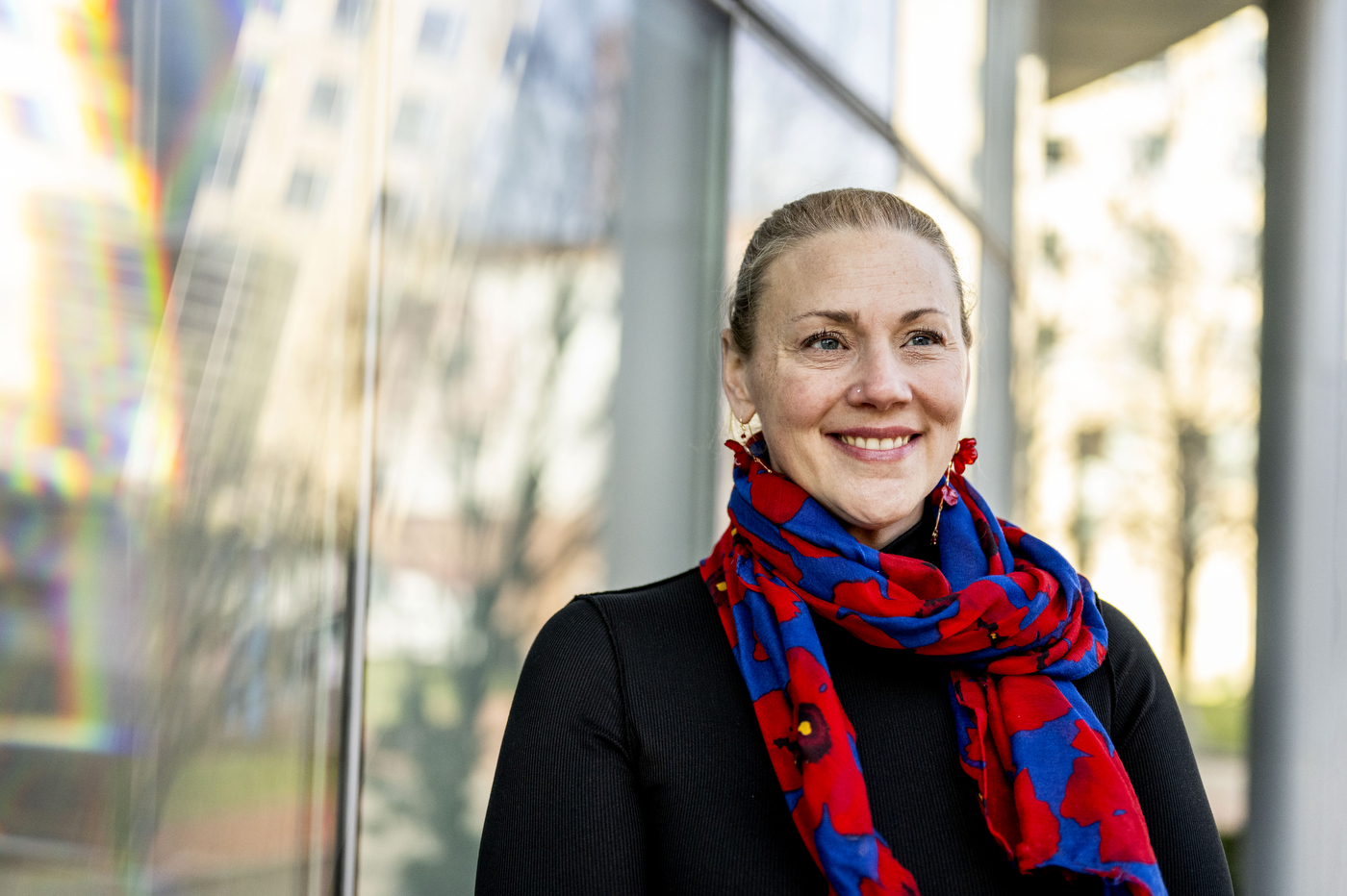 Michelle Carr smiles while framed against a window, her blue and red scarf standing out against her black blouse.