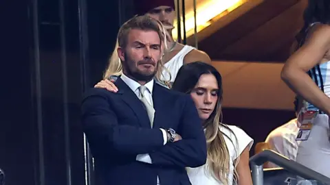 Shutterstock Sir David Beckham appears emotional with arms hands crossed following England's semi-final defeat. His wife Victoria has an equally sad expression and consoles him with an arm on his shoulder