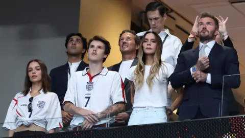Getty Images A picture of Jackie Apostel, Cruz Beckham, Victoria Beckham, David Beckham and Ken Paves in a box at a football match during the World Cup between England and Argentina. The group, dressed in a mixture of England shits and formal clothing, appear to be looking up at a screen, which is out of shot.