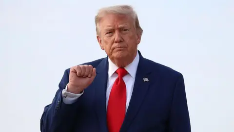 Getty Images Donald Trump holds up his right fist while wearing a white shirt and red tie.