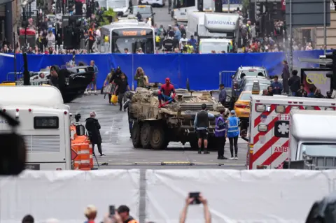 PA Media A street scene with Spiderman on top of a tank. Behind that is a blue screen, with a Glasgow bus beyond that