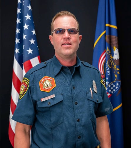 portrait man in tinted glasses and a blue button-down shirt with fire department patches, american and utah flags behind him
