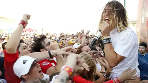 Getty Images Jared Leto, frontman for Thirty Seconds to Mars, performing in the open air to a crowd of people who are surging forwards. He is singing into a microphone and his hair is sweeping across his face (Photo by J. Shearer/WireImage)