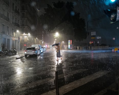 A person with an umbrella crosses a rain-soaked street at night