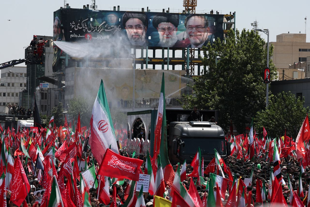 Water is sprayed to keep attendees cool as a vehicle carrying the coffins of Iran's late Supreme Leader Ayatollah Ali Khamenei and his family members drives through the crowded streets of Tehran.