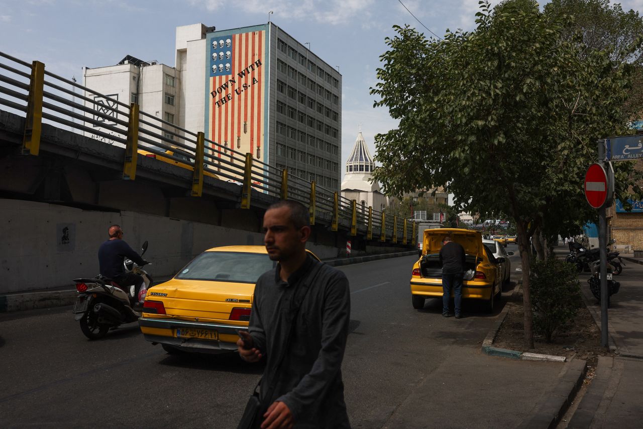 People walk the street with an anti-US mural on a building in the background, in Tehran, Iran, July 18.
