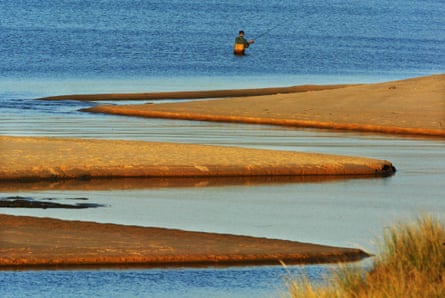 a person wades in water to fish with rod and line