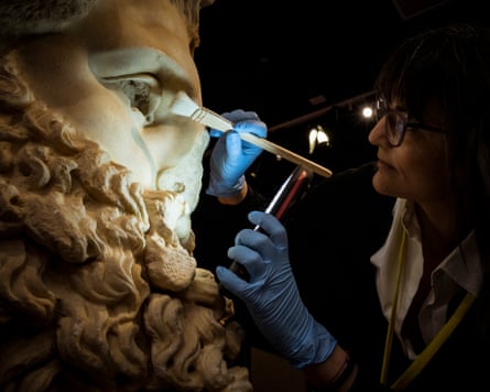A conservator with a torch and brush tends to a huge representation of Zeus’s head