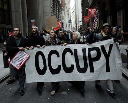 Protesters march along a street holding a banner reading ‘occupy’