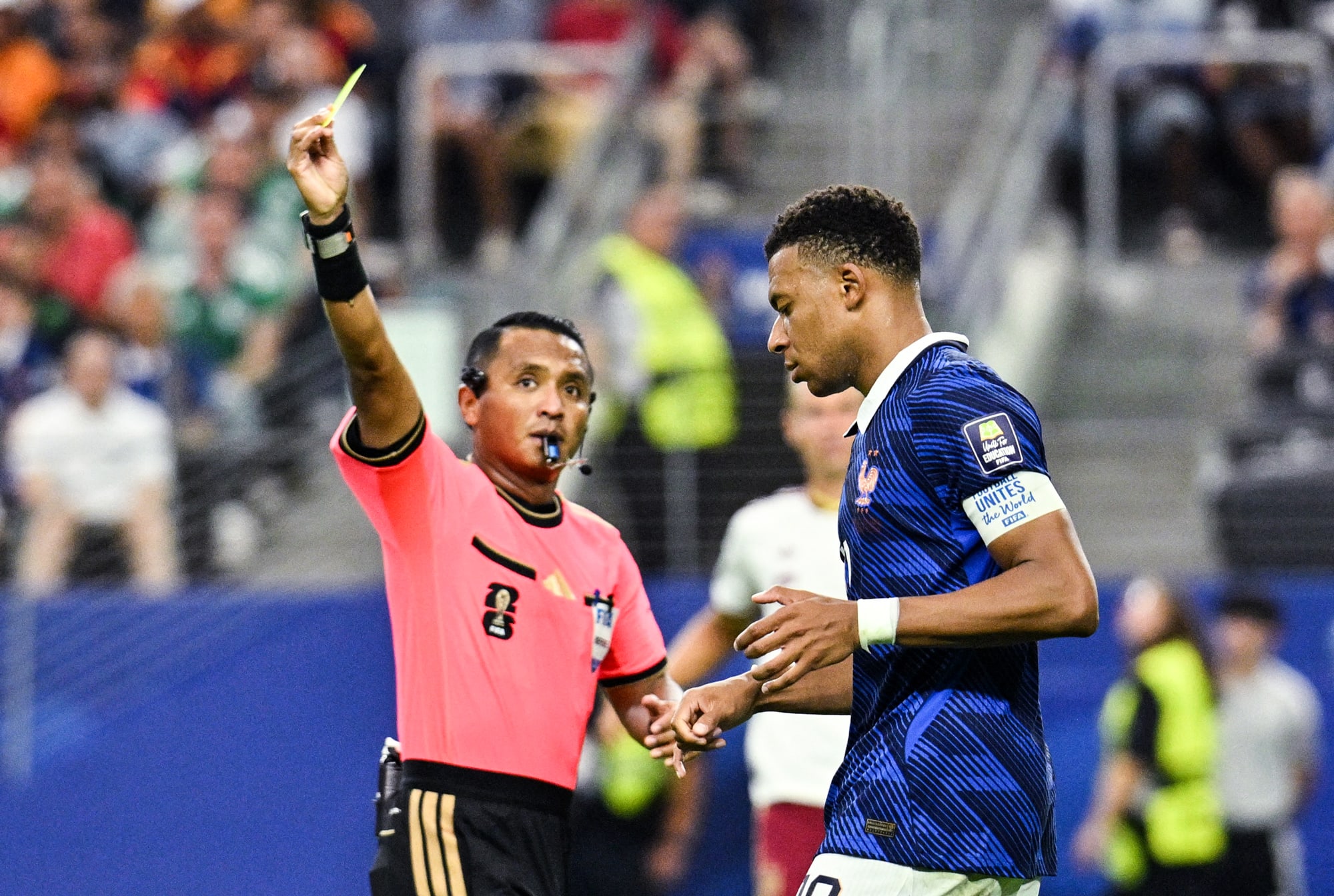 Kylian Mbappe is shown a yellow card by referee Ivan Barton on the soccer field