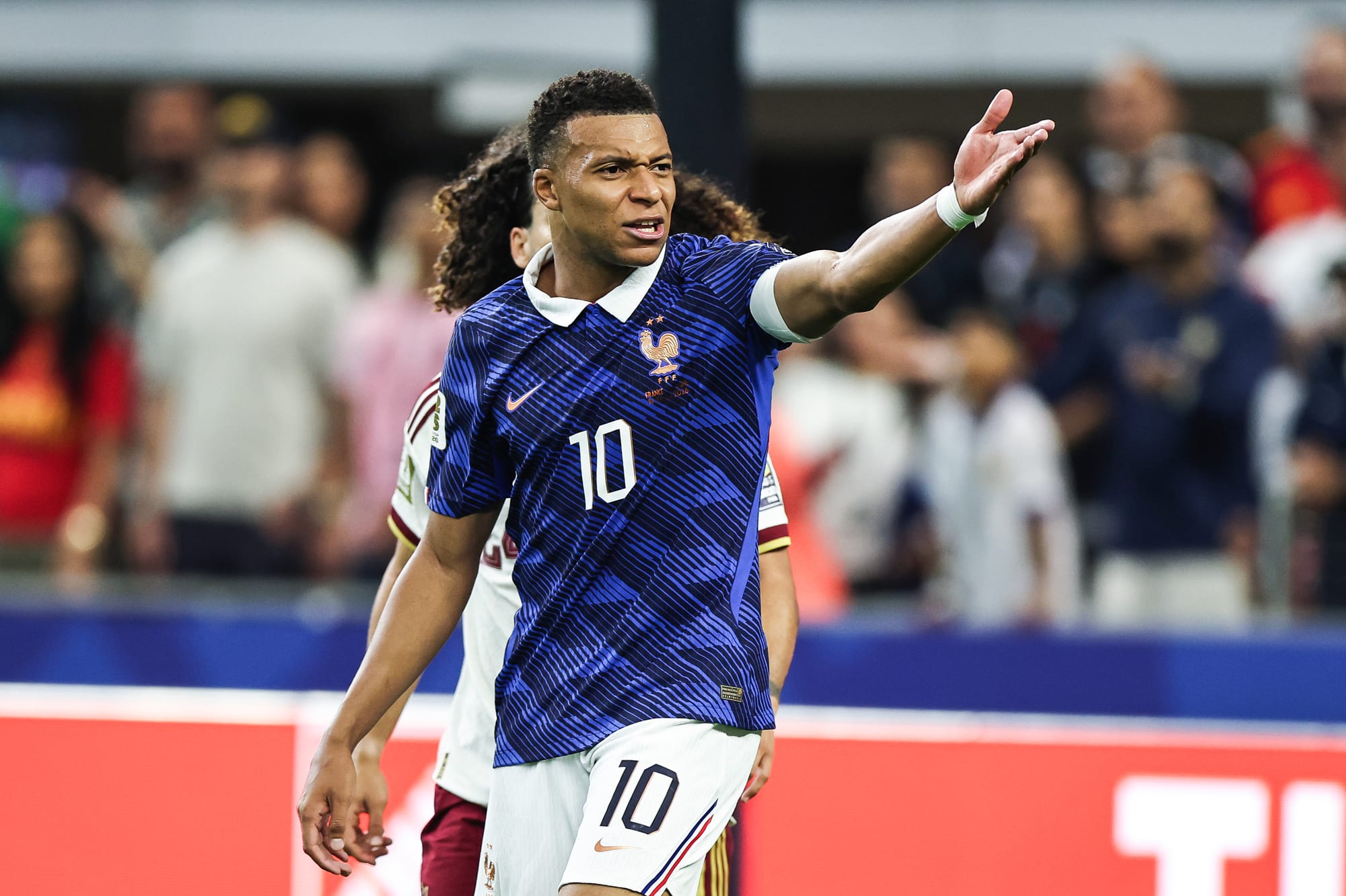Mbappe raises a hand outwards while yelling on the soccer field
