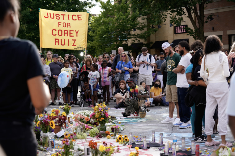 A makeshift memorial in an intersection with people crowded around it.