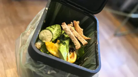 BBC An image of a food waste bin with bread and vegetables inside
