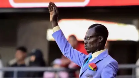 Getty Images Smartly-dressed Michel Kuka Mboladinga, better known as Lumumba Vea or the "living statue", stands still with his armed raised while watching his country DR Congo