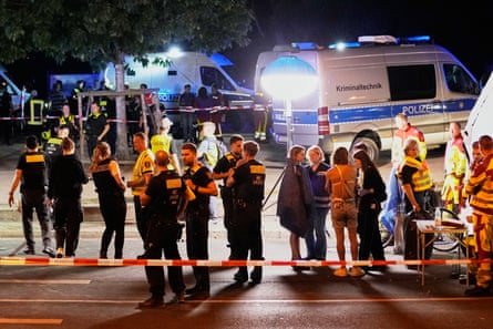 Emergency personnel and police gather in front of emergency vehicles and behind police tape at night