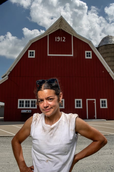 A young woman with long hair pinned up, white T-shirt with shoulders rolled up, in front of A-frame red bar with white letters at peak spelling “1912.”