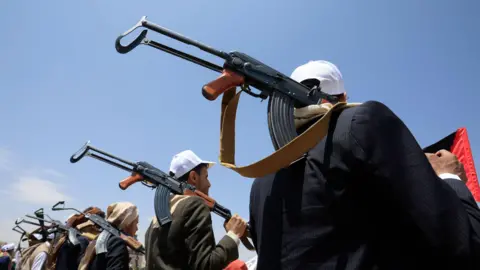 EPA Armed students participate in a rally supporting the Houthi-imposed naval embargo against Saudi Arabia in Sana'a, Yemen, 22 July 2026. Hundreds of students gathered at Sanaa University to support the declaration. The students are seen from behind, holding assault rifles over their shoulders, wearing white baseball caps