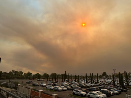 Smoke plumes rise from wildfires behind a road and car park