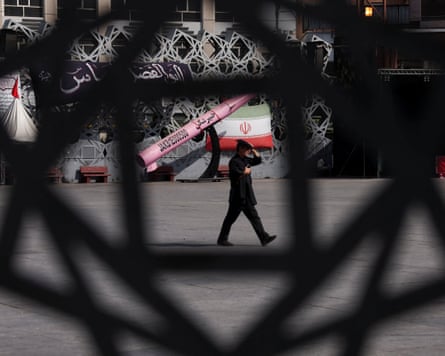 A man walks past a mockup of an Iranian missile and flag in Tehran