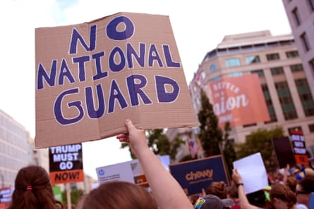 Demonstrators hold signs saying ‘No National Guard’ and ‘Trump Must Go Now’