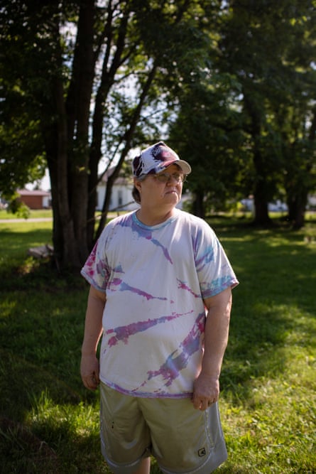 A woman in a tie-dyed shirt and hat stands near trees.