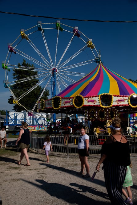 People gather at a small fair with a ferris wheel and carousel.