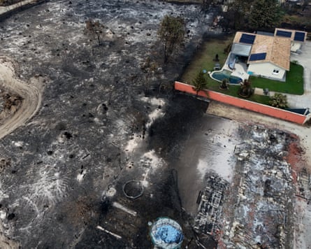 A burnt and razed area of land with just one house untouched in one corner of the image
