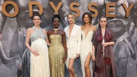 Getty Images Anne Hathaway, Lupita Nyong'o, Charlize Theron, Zendaya and Samantha Morton standing in a row in designer outfits in front of a large sign saying "Odyssey" at the premiere in New York on 14 July 2026