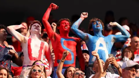 Getty Images Three men paint their upper bodies in white, red and blue body paint that reads USA as they cheer from the stands at Los Angeles stadium before the FIFA World Cup 2026 Group D match between Türkiye and USA on 25 June 2026