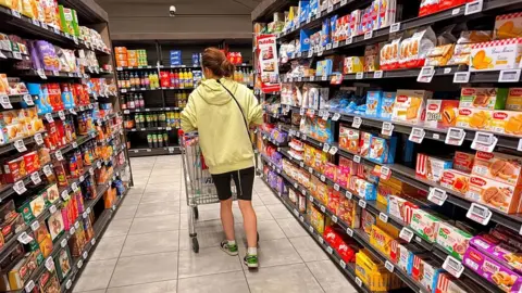AFP via Getty Images A woman shops pushes her shopping cart through a cake and biscuit aisle at an Intermarché  supermarket in France.