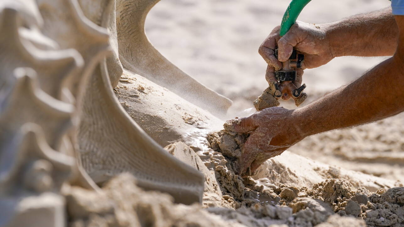 Right hand holding hose sprays water into left hand holding clump of sand