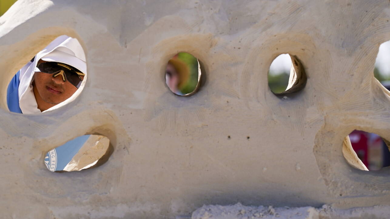 Man in blue shirt and white hood seen through hole in sand sculpture