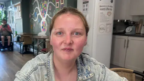 BBC Susan has blonde hair tied back and is wearing a blue denim jacket.