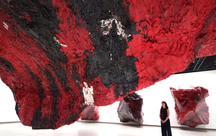 A woman gazes at a big black and red sculpture mounted on the ceiling