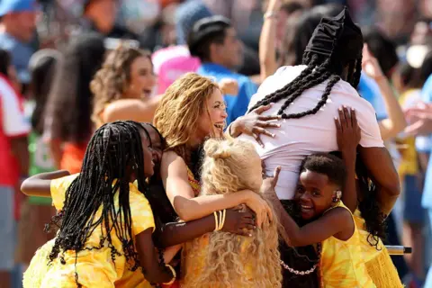 Getty Images for Global Citizen Shakira and Burna Boy hug Ghetto Kids after their routine at the World Cup final half-time show