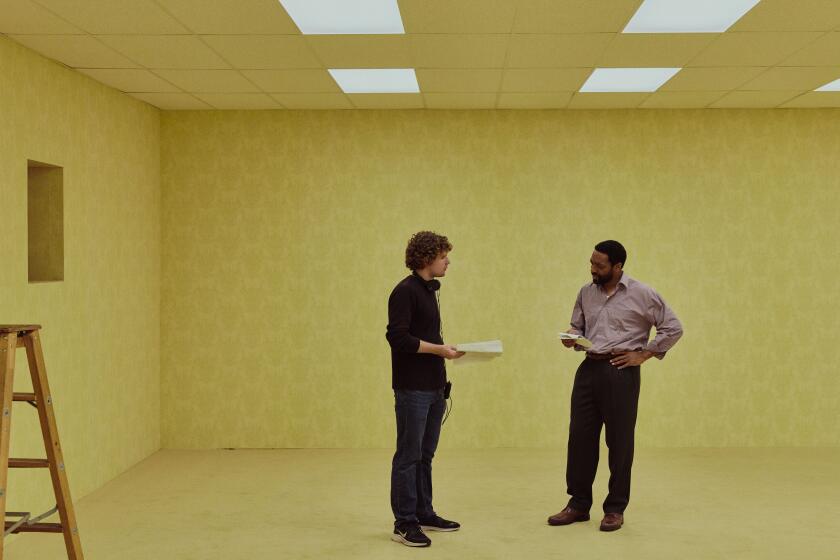 Two men have a discussion about a scene in a large yellow room.