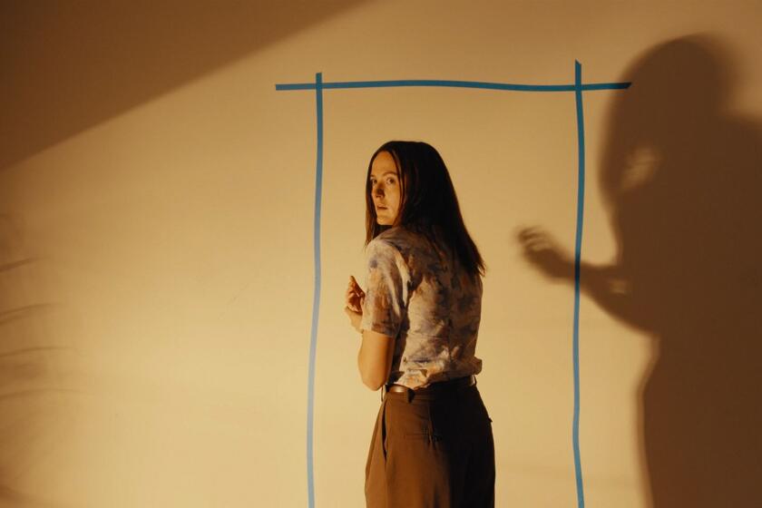 A woman stands in front of a wall with a taped outline of a doorway.