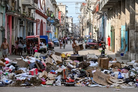 A woman holds a cardboard box in front of rubbish piled on a street in Havana