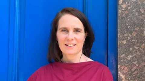 Siobhan has shoulder length dark hair and is wearing a pink top.