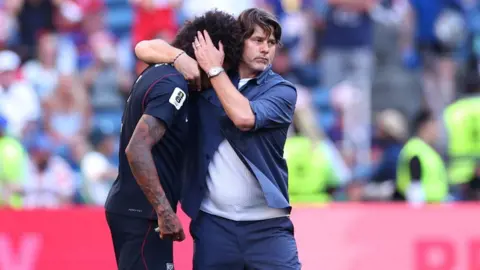 Getty Images Pochettino has his arm around the neck of Richards who has buried his head in the coach's shoulder. Pochettino's left hand is on the back of Richards' head as it to console him. The two men are on the football pitch and the crowd in the background are out of focus