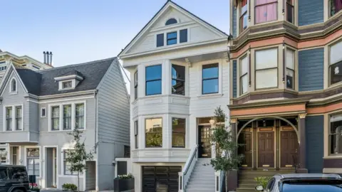 Open Homes Photography Three homes on a residential street in San Francisco. The three floor homes look clean and well maintained with well-trimmed plants and trees outside.