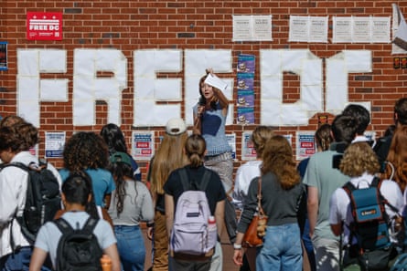 A woman speaks to a group of people in front of a brick wall with ‘Free DC’ spelled out in large letters.