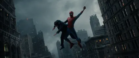Marvel/ Sony Pictures Entertainment Spider-Man swinging through high-rise buildings, carrying a person over one arm