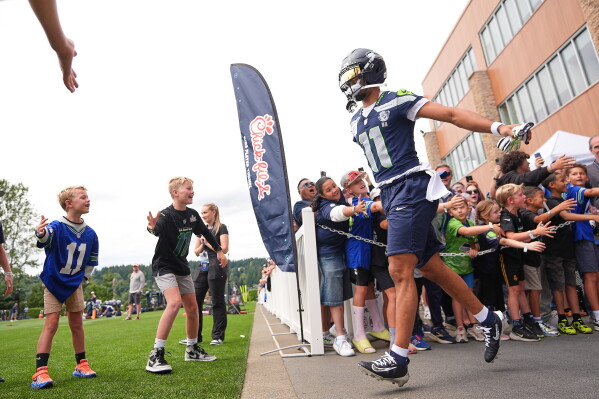 Seattle Seahawks wide receiver Jaxon Smith-Njigba greets young fans as he runs out during the NFL football team's training camp, Sunday, July 26, 2026, in Renton, Wash. (AP Photo/Lindsey Wasson)