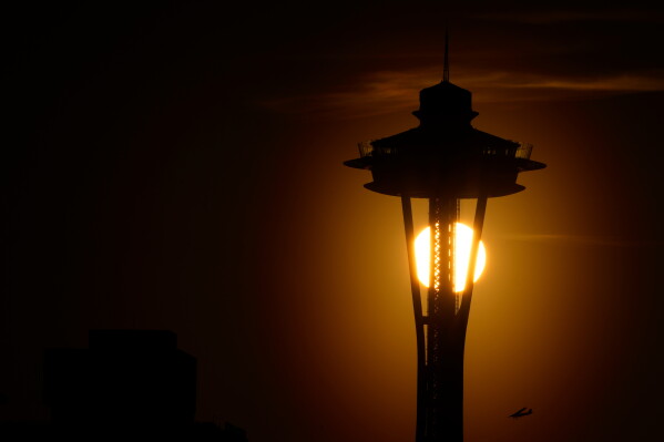 The sun sets behind the Space Needle as a small plane flies by on the first day of spring, Tuesday, March 19, 2024, in Seattle. (AP Photo/Lindsey Wasson,File)