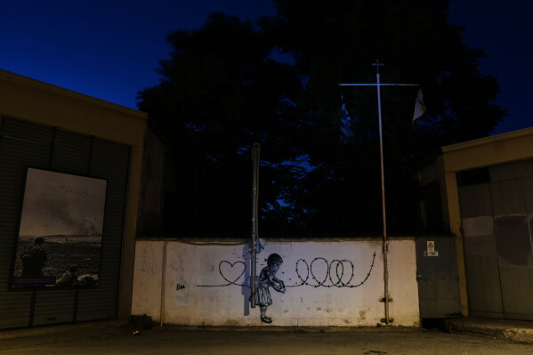 Graffiti depicting a girl painting barbed wire into a heart covers a wall along a blocked road separating the Greek Cypriot south from the Turkish Cypriot north, along the U.N.-controlled buffer zone established after the July 20, 1974 Turkish invasion of Cyprus, in the medieval core of the divided capital, Nicosia, Cyprus, on July 13, 2026. (AP Photo/Petros Karadjias)