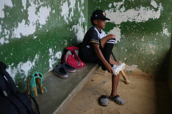 Yeferson Seijas puts his cleats on for baseball practice in La Guaira, Venezuela, Saturday, July 11, 2026, after the earthquakes left his family without a home and some of the boys he grew up playing with injured, orphaned, dead or missing. (AP Photo/Ariana Cubillos)