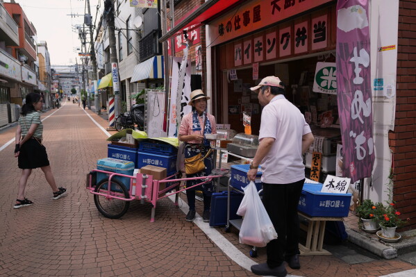 Akiko Sugaya helps a customer asking for tofu at her takeout lunch shop, which turns into a dine-in restaurant in the evening, before she starts peddling with her cart in Tokyo, Saturday, July 4, 2026. (AP Photo/Hiro Komae)