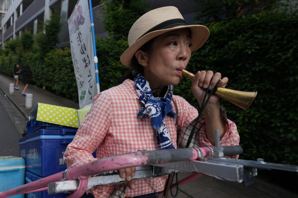 Akiko Sugaya blows an old-style horn while she peddles tofu, prepared food and beverages in a cart in Tokyo, Saturday, July 4, 2026. (AP Photo/Hiro Komae)