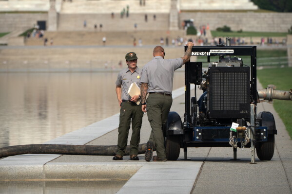 National Park Service workers stand near a pump placed next to the Lincoln Memorial Reflecting Pool, Friday, July 10, 2026, in Washington. (AP Photo/Mark Schiefelbein)